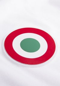 Witte stof met een cirkelvormige patch met een rode buitenring, een witte middenring en een centrale groene cirkel. Glad textuur.