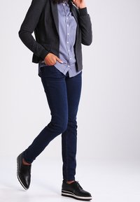 Dark gray blazer, light blue button-up shirt, dark blue skinny jeans, and black shoes with white stripes. Smooth textures and fitted design.