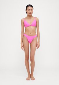Rožinės juostelės bikini komplektas, kuriame yra trikampis bikini viršus su reguliuojamomis petnešėlėmis ir atitinkamos žemos juosmens kelnaitės, viskas ryškiame atspalvyje.