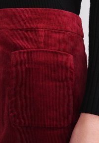Falda de pana roja con un bolsillo frontal destacado y una textura de acanalado vertical. La cintura está ligeramente fruncida para un aspecto ajustado.