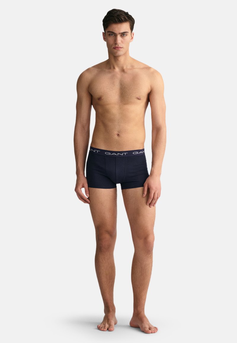 Kratke hlače od pamuka u mornarsko plavoj boji s elastičnom trakom u struku, na kojoj se ponavlja logo "GANT". Uski kroj, glatka tekstura. Model stoji bose noge.