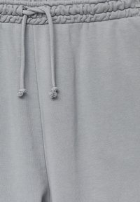 Jasnoszare spodnie dresowe z elastycznym pasem i sznurkiem do regulacji. Materiał wydaje się miękki, o gładkiej fakturze i minimalnej liczbie widocznych szwów.