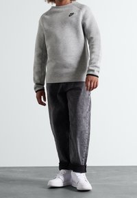 Grå sweatshirt med rund hals, texturerad tyg och svart logotyp, som kombineras med svarta utblekta jeans och vita sneakers med svarta detaljer.