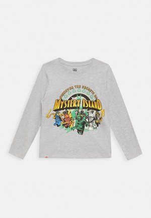 Lysegrå langærmet skjorte med farverig tekst "Mystery Island" og fem tegneserie-ninjafigurer i actionstillinger på forsiden.