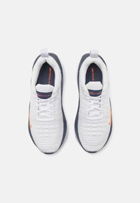 Białe buty sportowe z textured górą, granatową podeszwą i jasnopomarańczowymi akcentami po bokach. Posiadają sznurowanie i uchwyt do zakupu.