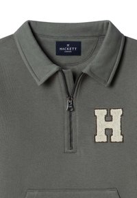 Jersey verde con cuello con cremallera, con un parche beige en forma de "H". Fabricado con tela suave y de textura lisa. Diseño de ajuste estándar.