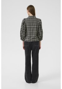 Cămașă în carouri alb-negru cu mâneci pufoase, asortată cu pantaloni din denim închis la culoare, cu talie înaltă, care au buzunare laterale și cusături pe spate.