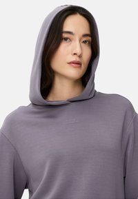 Paarse hoodie met een zachte textuur, voorzien van een grote capuchon en minimalistische geborduurde tekst "MADE FOR DAILY ADVENTURES" op de borst.