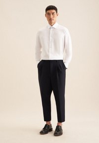 Weißes Hemd mit langen Ärmeln, kombiniert mit hoch taillierten, dunkelblauen Hosen und schwarzen Schnürschuhen. Einfaches Design, keine Muster.