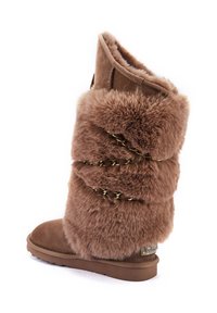 Smeđe visoke čizme s mekanom krznom, ravnim đonom i ukrasnim lancima omotanim oko nogavice, sa logotipom sa strane.