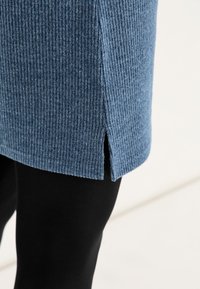 Blaue gerippte Strick-Tunika mit seitlichen Schlitzen am Saum, kombiniert mit schwarzen Leggings. Sie verfügt über einen strukturierten Stoff und einen lässigen Schnitt.