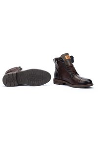 Brown leather ankle boots with a rounded toe, lace-up front, and zipper closure. Textured rubber sole with tread patterns. Brown and green accents.