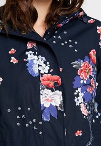 Marineblå jakke med blomsterprint lavet af letvægtsstof, der har store flerfarvede blomster og subtile prikker som accent på stoffet.