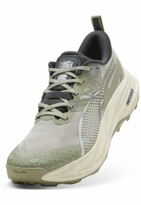 Zapatilla deportiva ligera con parte superior de malla en gris claro y acentos en verde oliva, entre suela blanca gruesa y suela de goma texturizada.