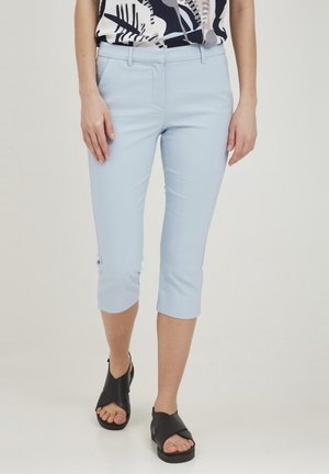 Lyseblå cropped bukser lavet af et glat stof, med et klassisk design med flad front og oplagte manchetter. Parret med sorte sandaler.