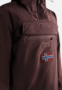 Veste marron foncé avec poche zippée à l'avant et écusson du drapeau norvégien sur la poitrine.
