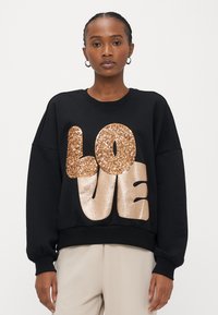 Sweatshirt preta com texto "LOVE" em glitter dourado oversized. Apresenta gola redonda e mangas com punhos, feita de tecido macio.