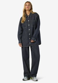 Temno denim prevelik jopič z zaponko na gumbe in dvema sprednjima žepoma, kombiniran z ujemajočimi se širokimi hlačami in športnimi sivimi supergami.