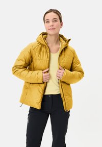 Giacca imbottita gialla con cappuccio, dotata di zip frontale, polsini elasticizzati e design leggero. Indossata sopra una maglietta gialla chiara e pantaloni scuri.