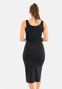 Vestido midi negro, sin mangas, ajustado al cuerpo, con escote redondo, textura suave, silueta ceñida y sin patrones ni acentos visibles.