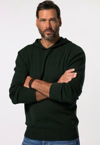 Dunkelgrüner Kapuzenpullover mit gerippten Bündchen und Saum, ausgestattet mit einem strukturierten Stoff und einem kleinen schwarzen Logo-Patch an der Unterseite.