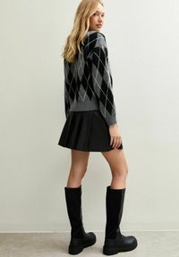 Grau gestrickter Pullover mit Argyle-Muster in Schwarz und Weiß, kombiniert mit einem schwarzen, gefältelten Rock und kniehohen schwarzen Stiefeln. Glatte Texturen sind deutlich erkennbar.