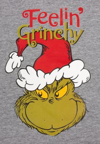 T-shirt grigia con un personaggio dei cartoni animati verde che indossa un cappello di Babbo Natale rosso con bordo bianco. La scritta dice "Sentirsi Grinch" in rosso e oro.