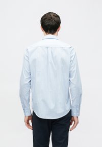 Jasnoniebieska koszula w paski z długim rękawem, wykonana z bawełny, z kołnierzykiem zapinanym na guziki i zaokrąglonym dołem. Mankiety zapinane na guziki.