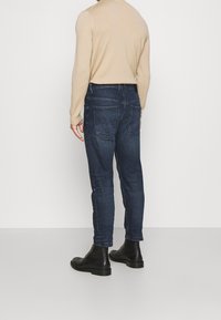 Mörkblå denimjeans med slim fit, utrustade med bakfickor och minimala sömdetaljer, tillsammans med svarta ankelstövlar.