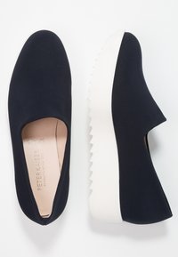 Zwarte instapschoenen met een gladde bovenkant, voorzien van een brede opening en een witte kartelrand zool. De binnenkant is beige met merkdetails.