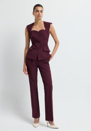 Gilet bordeaux su misura con scollo quadrato e tre bottoni, abbinato a pantaloni slim-fit coordinati, con tasche frontali e una texture liscia.