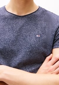 Námořnická modrá košile s texturovanou tkaninou, kulatým výstřihem a malým vyšitým logem na prsou. Krátké rukávy, volný střih.