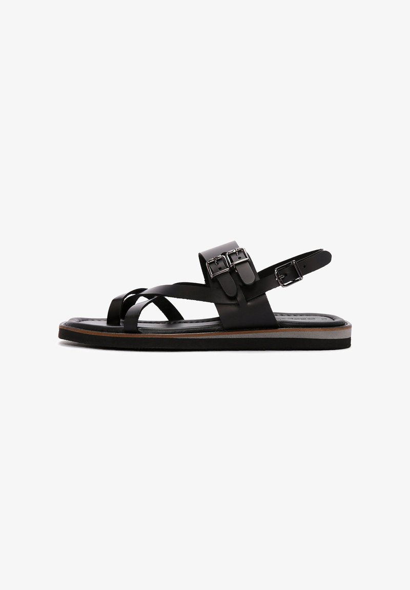 Black leather sandals feature crisscross straps, adjustable buckle closure, and a flat sole with a slight tan accent. Smooth texture.