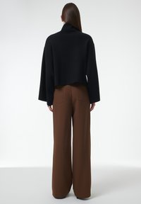 Schwarzer, verkürzter Pullover mit hohem Kragen und weiten Ärmeln, kombiniert mit braunen, hoch taillierten, weit geschnittenen Hosen mit Gesäßtaschen.