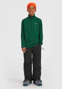 Groene fleece trui met rits en O'Neill-logo, gecombineerd met zwarte skibroek en grijze skischoenen. Model draagt een oranje muts.