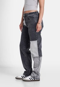 Jeans in denim grigio con un design a patchwork, caratterizzati da una combinazione di sezioni grigie scure e chiare. Lunghezza completa con taglio dritto.