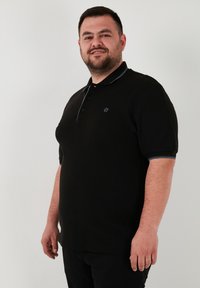 Čierne polo tričko s krátkymi rukávmi, s golierom a malým logom na hrudi. Šedé akcenty na golieri a zakončení rukávov.