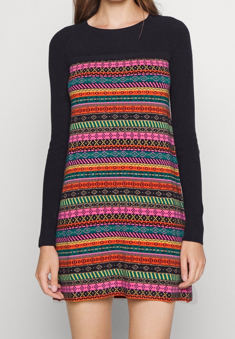 Femme portant une robe noire à manches longues avec des rayures horizontales colorées à motifs rose, orange, vert et bleu sur le devant.