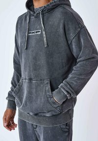 Sweatshirt à capuche gris foncé avec une finition texturée et délavée. Comprend une poche kangourou, des poignets côtelés et un logo sur la poitrine.