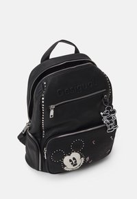 Schwarzer Kunstleder-Rucksack mit Reißverschlüssen, Nietenakzenten, einem Mickey Mouse-Print und einem baumelnden Mickey-Schlüsselanhänger.