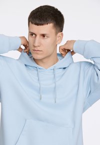 Felpa azzurra chiara realizzata in tessuto morbido, con tasca a marsupio e coulisse regolabile con estremità metalliche. Logo ricamato sul petto.