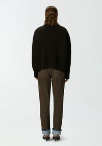 Crni rebrasti oversized pulover, opuštenog kroja, uparen s tamnosmešnim hlačama, s manžetama na rubovima, u kombinaciji s crnim štiklama.