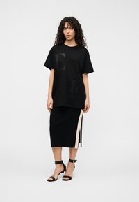 Μαύρο βαμβακερό μπλουζάκι με μεγάλα υφασμάτινα γράμματα "E" και "F", σε συνδυασμό με μαύρη pencil φούστα με πλαϊνή σχισμή και διακριτική λεπτομέρεια από λουράκι σε αντίθετο χρώμα.