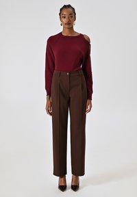 Maglione borgogna con dettaglio sulle spalle scoperte, abbinato a pantaloni marroni a vita alta e tacchi a punta neri, offrendo una texture liscia.