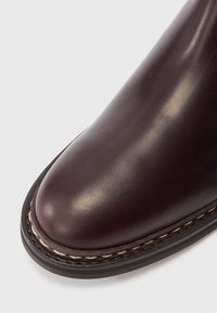 Gros plan sur la pointe d'une botte en cuir marron foncé lisse avec des coutures détaillées de couleur claire sur la semelle noire.