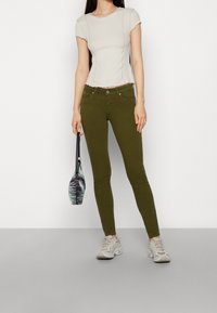 Olivově zelené skinny džíny s předními kapsami, doplněné o světlý béžový top s fitted střihem, který má žebrovanou texturu a kulatý výstřih.