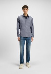 Donkerblauw geruite overhemden met lange mouwen, met een spread collar en een klein logo. Gecombineerd met lichtblauwe spijkerbroek en sneakers.