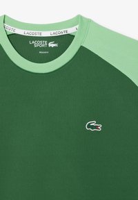 Tricou sportiv Lacoste verde, cu o croială normală, guler rotund și mâneci contrastante de un verde deschis, având logo-ul cu crocodil pe piept.