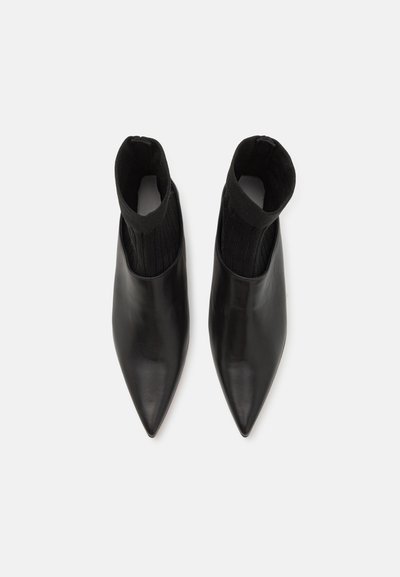 Melnas ādas potīšu zābaki ar smailu purngalu un adītu melnu zeķes stila detaļu augšpusē. Gluda virsma bez redzamiem rakstiem.