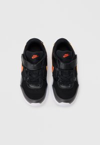 Fekete Nike sportcipők hálós és szintetikus felsőrészével, narancs részletekkel, állítható pánttal és fehér gumitalppal, lekerekített orrkialakítással.